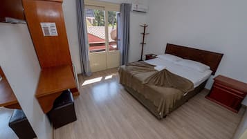 A hotel room with a bed, a wooden wardrobe, a small bedside table, a heater, and a view of the outside.