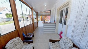 A covered outdoor seating area with wooden benches and a table with magazines, a reception desk, and a view of the street. - Pousada Prime Gramado (Gramado)
