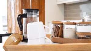Una encimera de cocina con una cafetera, una taza blanca y botes de azúcar y ramas de canela.