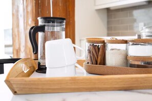 Un piano di lavoro in cucina con una moka, una tazza bianca e barattoli di zucchero e stecche di cannella.