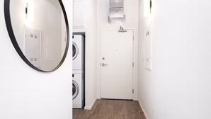 Un lavadero con una puerta blanca, una lavadora y un espejo en la pared.