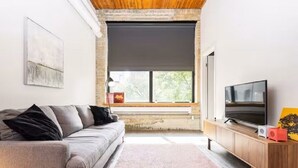 Una sala de estar con sofá, televisor y ventana con vistas a zonas verdes.