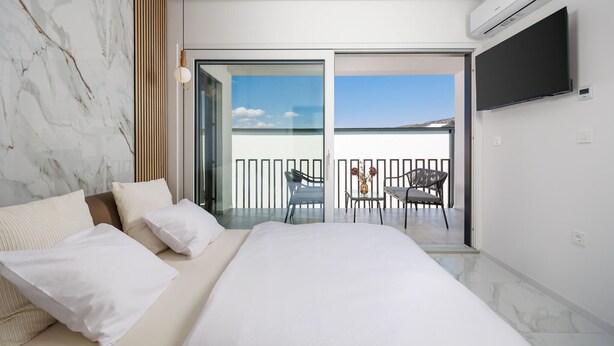 A modern bedroom with a large bed, a balcony with a table and chairs, and an air conditioning unit. - Nice home in Jadranovo (Jadranovo)