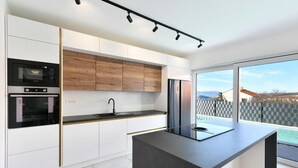 A modern kitchen with white cabinetry, a built-in oven, a microwave, and a large island with a sink. - Pet friendly home in Jadranovo with sauna (Jadranovo)
