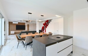 A modern kitchen with a central island, a dining area with a long table and chairs, and a living area with a sofa and TV. - Pet friendly home in Jadranovo with sauna (Jadranovo)