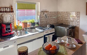 A kitchen with a gas stove, a kettle, and a coffee maker. There are potted plants on the windowsill and a bowl of oranges on the counter. - Awesome home in Crni Lug with WiFi (Crni Lug)