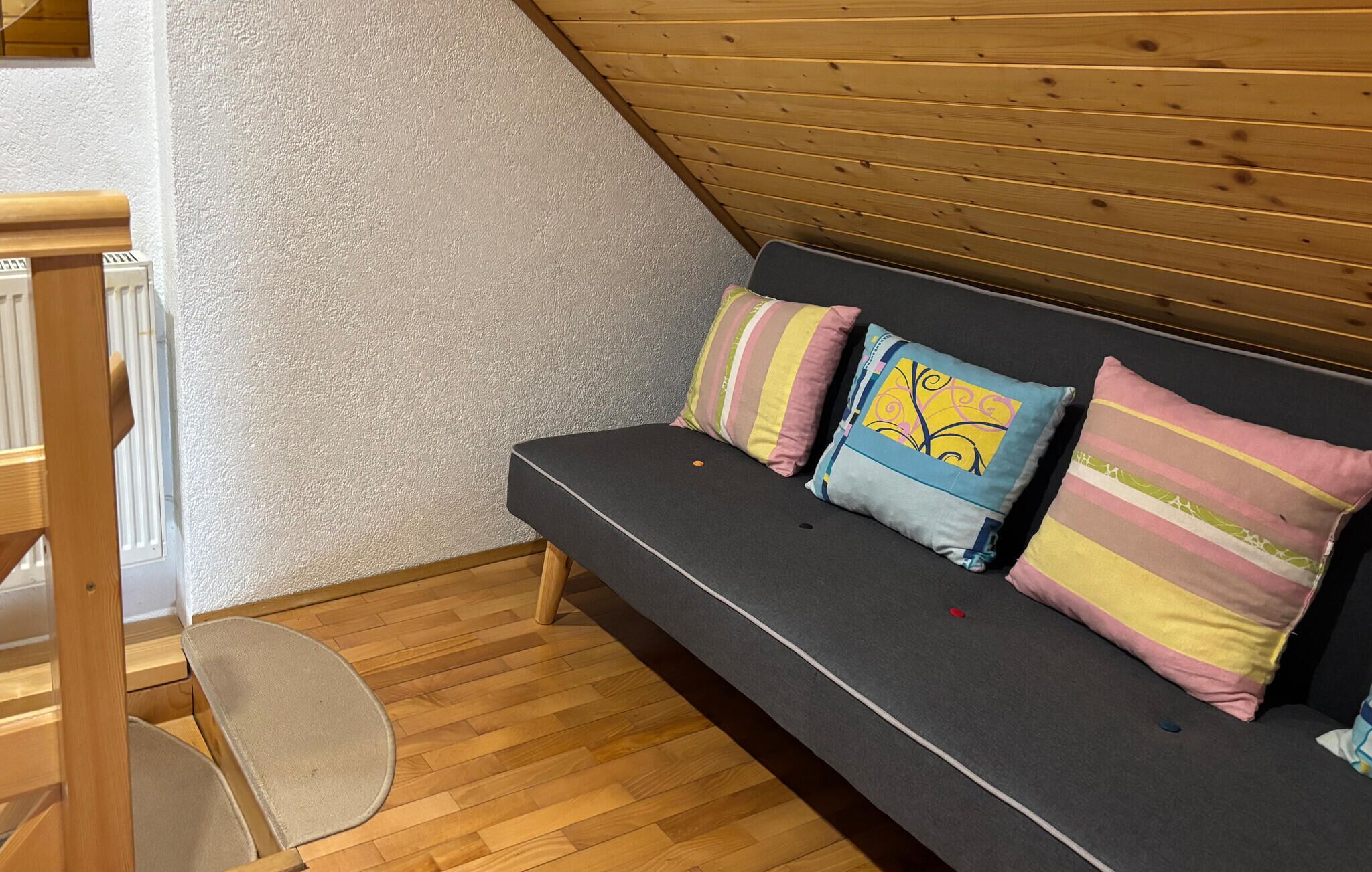 A cozy room with a dark grey sofa, wooden flooring, and a sloped ceiling.