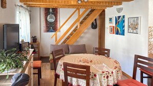 Ein gemütlicher Essbereich mit einer Holztreppe, einem Tisch mit Blumenmuster-Tischdecke und einem Fernseher links.