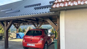 Ein rotes Toyota Auto steht unter einer hölzernen Konstruktion mit Metallverkleidung, umgeben von Kies und Bäumen.