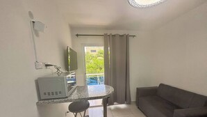 Une petite pièce avec un coin cuisine, un canapé, une chaise et une vue sur la verdure.