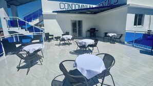 Une terrasse sur le toit, aménagée avec des espaces de détente en plein air et un barbecue, avec, en arrière-plan, un bâtiment portant l’inscription « CABINETS DENTAIRES EN COPROPRIÉTÉ ».