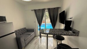 Un espace de vie compact comprenant un canapé, une petite table, un téléviseur et une fenêtre avec des rideaux.