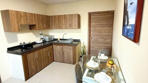 Een kleine keuken met houten kastjes, een inbouwfornuis en een eethoek met een glazen tafel gedekt voor twee personen.