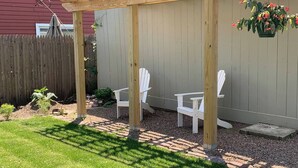 Una terraza de madera con sillas Adirondack, una maceta colgante y una valla de madera al fondo.