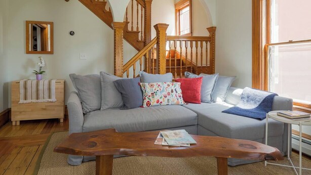 Un salón con un sofá seccional gris, una mesa de centro de madera y una escalera con barandillas de madera.