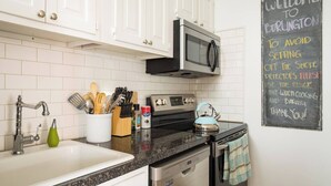 Una cocina con armarios blancos, un microondas, una estufa y un fregadero. Hay una pizarra con un mensaje sobre detectores de humo.