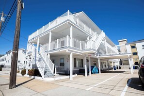 Un edificio de varios pisos con fachada blanca, un balcón en el segundo nivel y una escalera que conduce a la entrada.