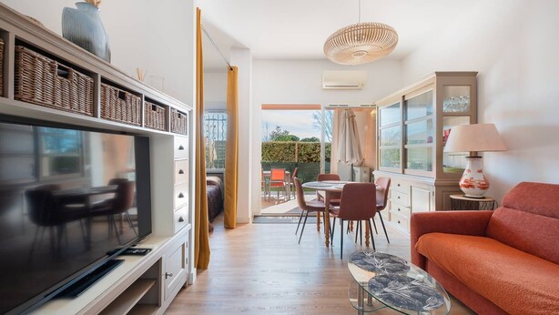 Ein modernes Wohnzimmer mit Fernseher, Sofa, Essbereich und Blick ins Freie.