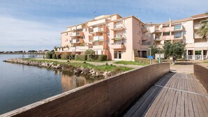 Ein Apartmentkomplex am Wasser mit Balkonen, einer Holzpromenade und ruhigem Gewässer.