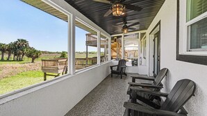 Une véranda couverte avec un ventilateur de plafond, des sièges d’extérieur et une vue sur le paysage.