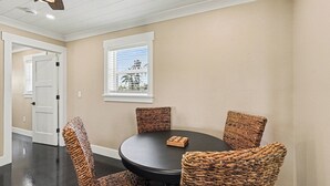 Un coin repas avec une table ronde et quatre chaises en osier, un ventilateur de plafond et une fenêtre avec des stores.