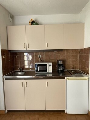 A compact kitchen with beige cabinets, a microwave, a coffee maker, and a refrigerator. - Apartment Héliopolis J 42 - 5 people (AGDE)