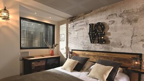 A bedroom with a large bed, a wall-mounted light sign, a window with blinds, and a rustic wall texture. - CAP FACTORY - Studio Héliopolis K 1 with garage - Luxe - 2 people (AGDE)