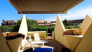 A covered outdoor seating area with white chairs and a blue table, overlooking a landscaped garden and buildings in the background. - CAP FACTORY - Studio Héliopolis K 1 with garage - Luxe - 2 people (AGDE)