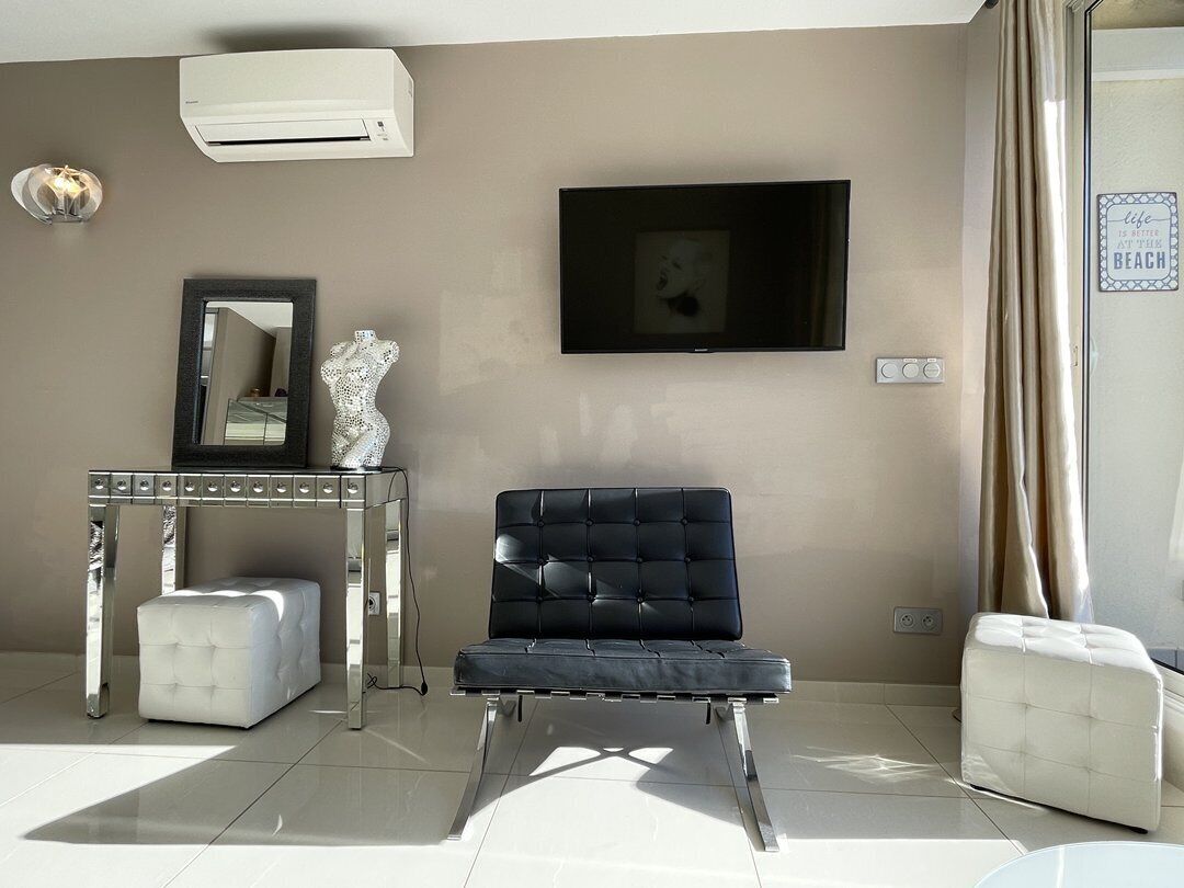 A modern living room with a black sofa, a white ottoman, a mirrored console table, and a flat-screen TV mounted on the wall.