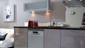 A modern kitchen with a dishwasher, a built-in oven, and a microwave. There is a coffee machine on the counter, and a painting is visible on the wall. - KERYLOS - Studio Héliopolis K 3 with garage - Luxe - 2 people (AGDE)