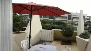 Une petite terrasse extérieure avec une table et des chaises, un parasol rouge et des plantes en pot.