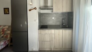 Une cuisine compacte équipée d’un réfrigérateur intégré, d’une cuisinière à gaz et de meubles de rangement en bois.