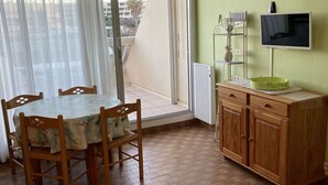 Ein Zimmer mit Esstisch und Stühlen, einem Holzschrank, einem Fernseher und einer Glastür zum Außenbereich.