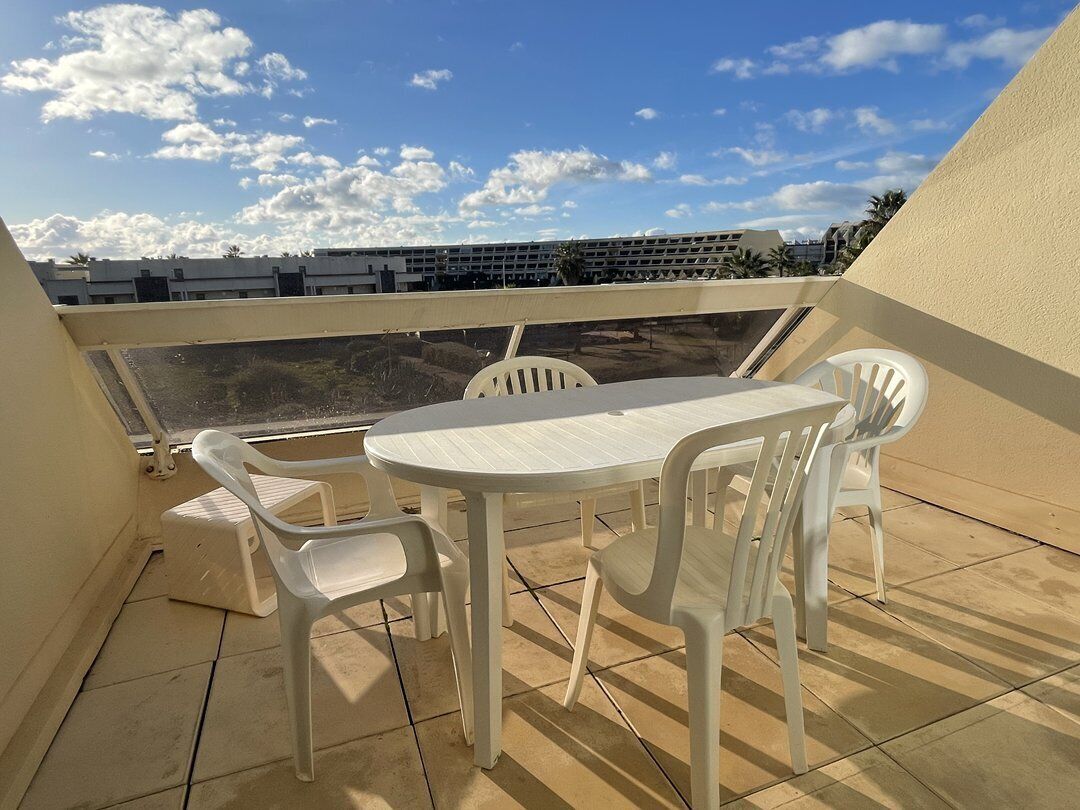 Un balcón con una mesa y sillas, vista de un edificio y cielo despejado.