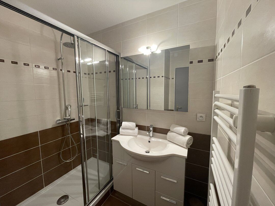 A bathroom with a glass shower enclosure, a sink with a mirror, and a towel rack.