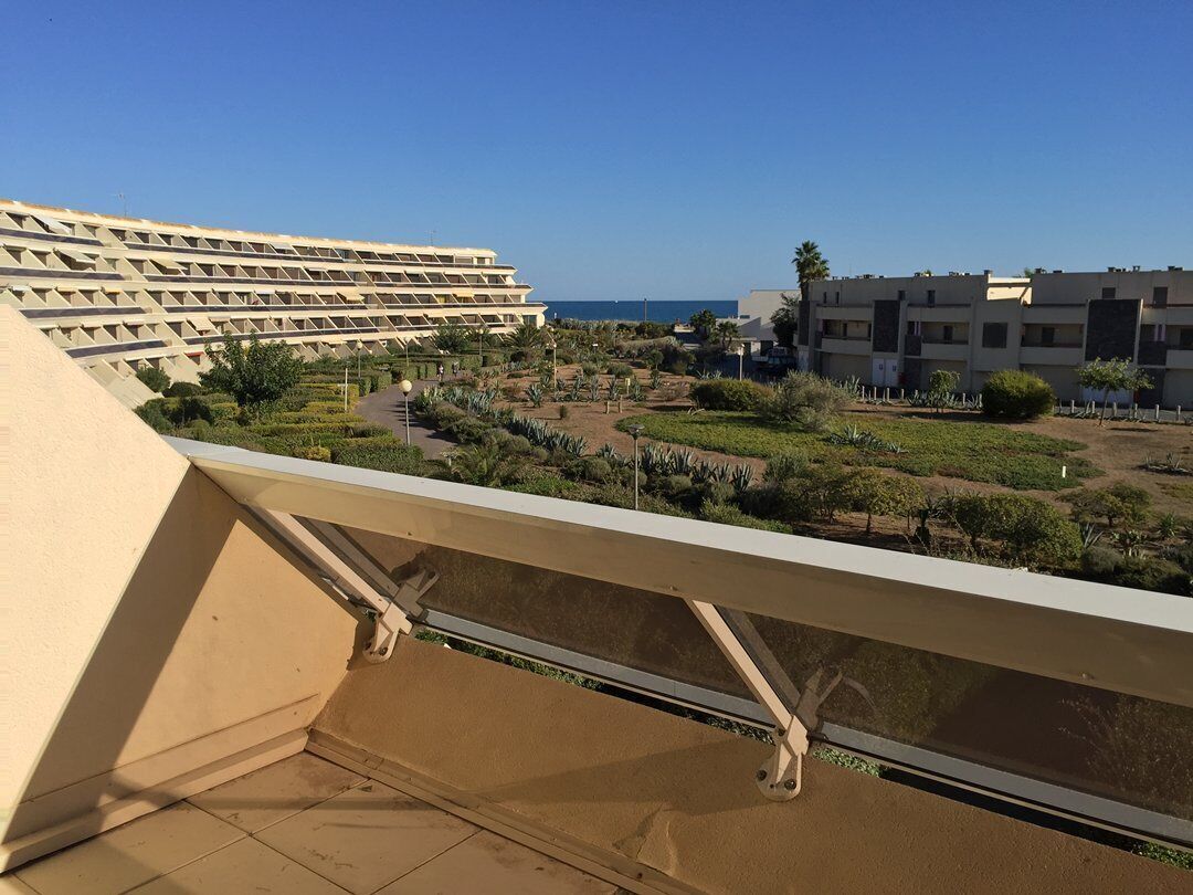 A balcony with a view of a residential area, including a building with a unique geometric facade and a clear blue sky.
