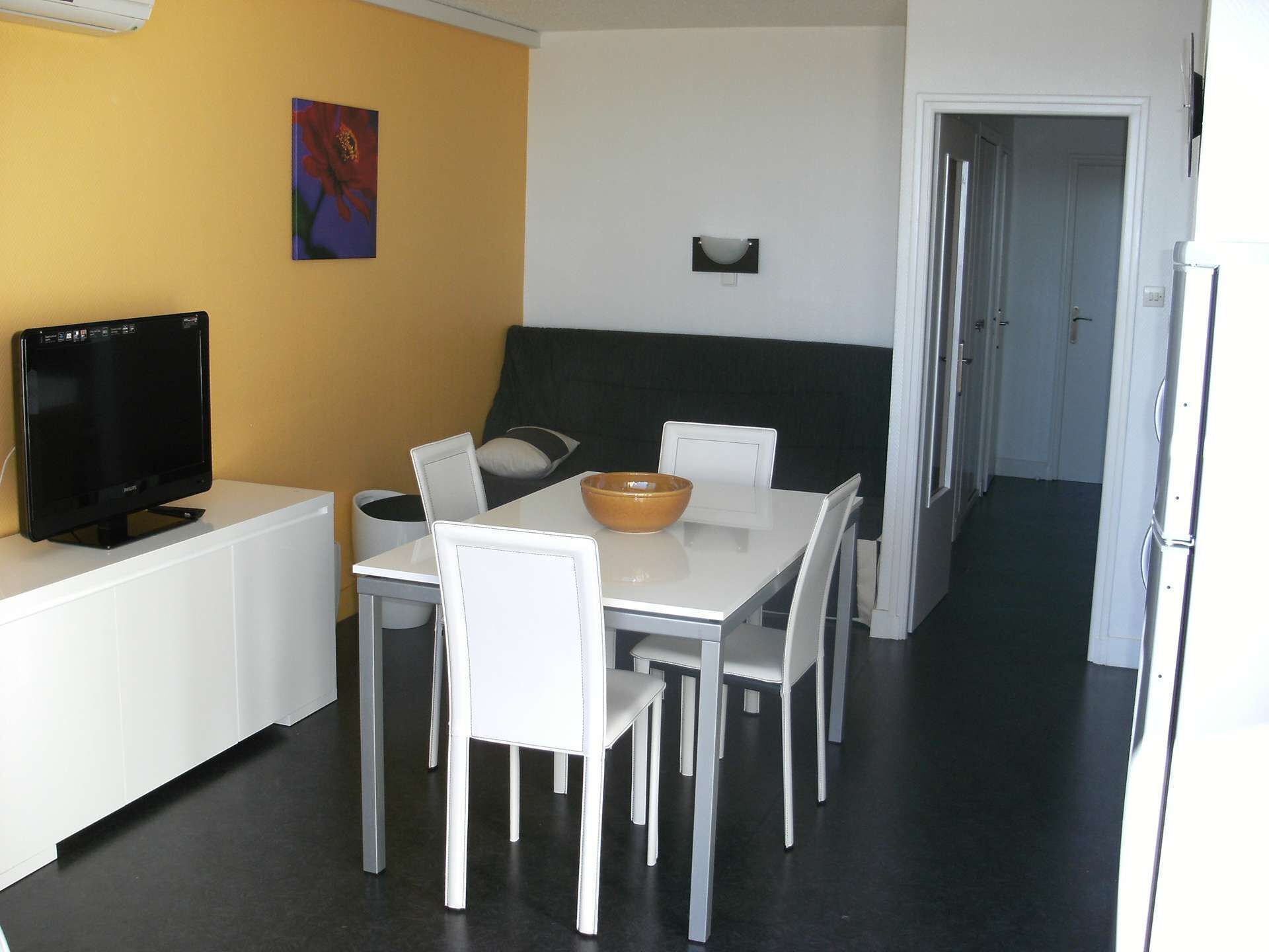 Ein kleiner Essbereich mit einem weißen Tisch, vier Stühlen, einer Schüssel und einem Flachbildfernseher auf einem weißen Schrank.