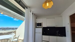 Een compacte keuken met witte kastjes, een zwart aanrechtblad en een magnetron. Er staat een eettafel met stoelen voor een raam met uitzicht op een stadsgezicht.