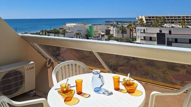 Een balkon met een tafel voor twee, met uitzicht op een strand en een resort.