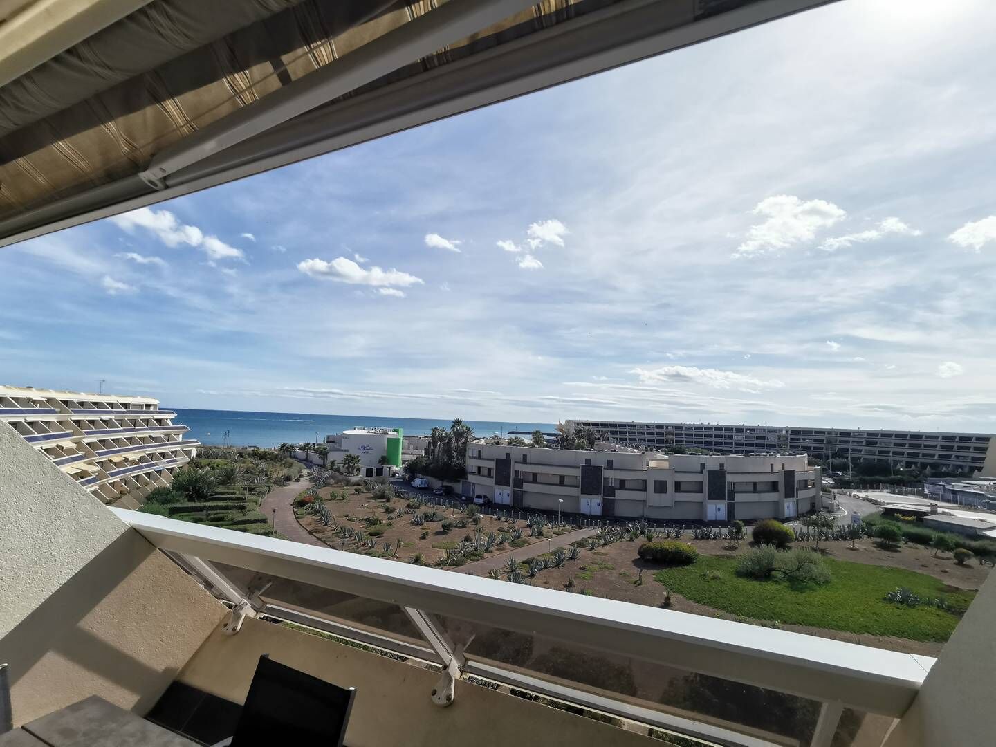 Vue depuis un balcon donnant sur un espace aménagé comprenant un bâtiment, un parking et une étendue d’eau.