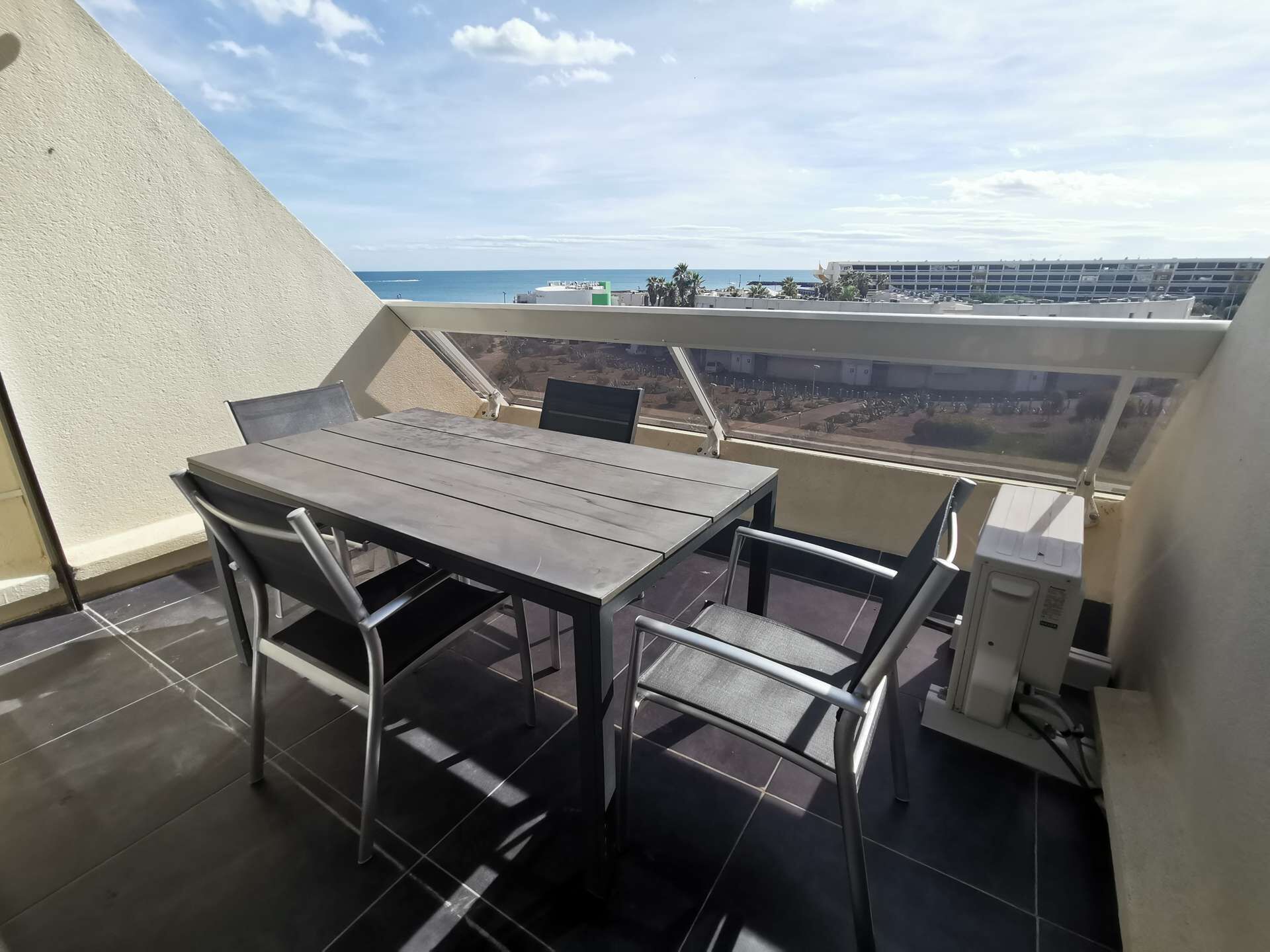 A balcony with a table and chairs, a view of the sea, and a building in the background.