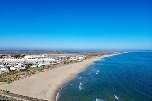Un hotel frente al mar con una extensa playa, cielo despejado y un edificio grande con múltiples balcones.