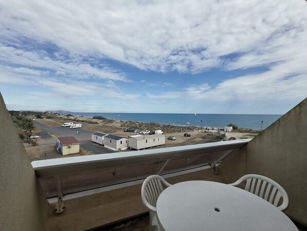 Un balcón con mesa y sillas, con vista a una playa con casas móviles y un cielo despejado.
