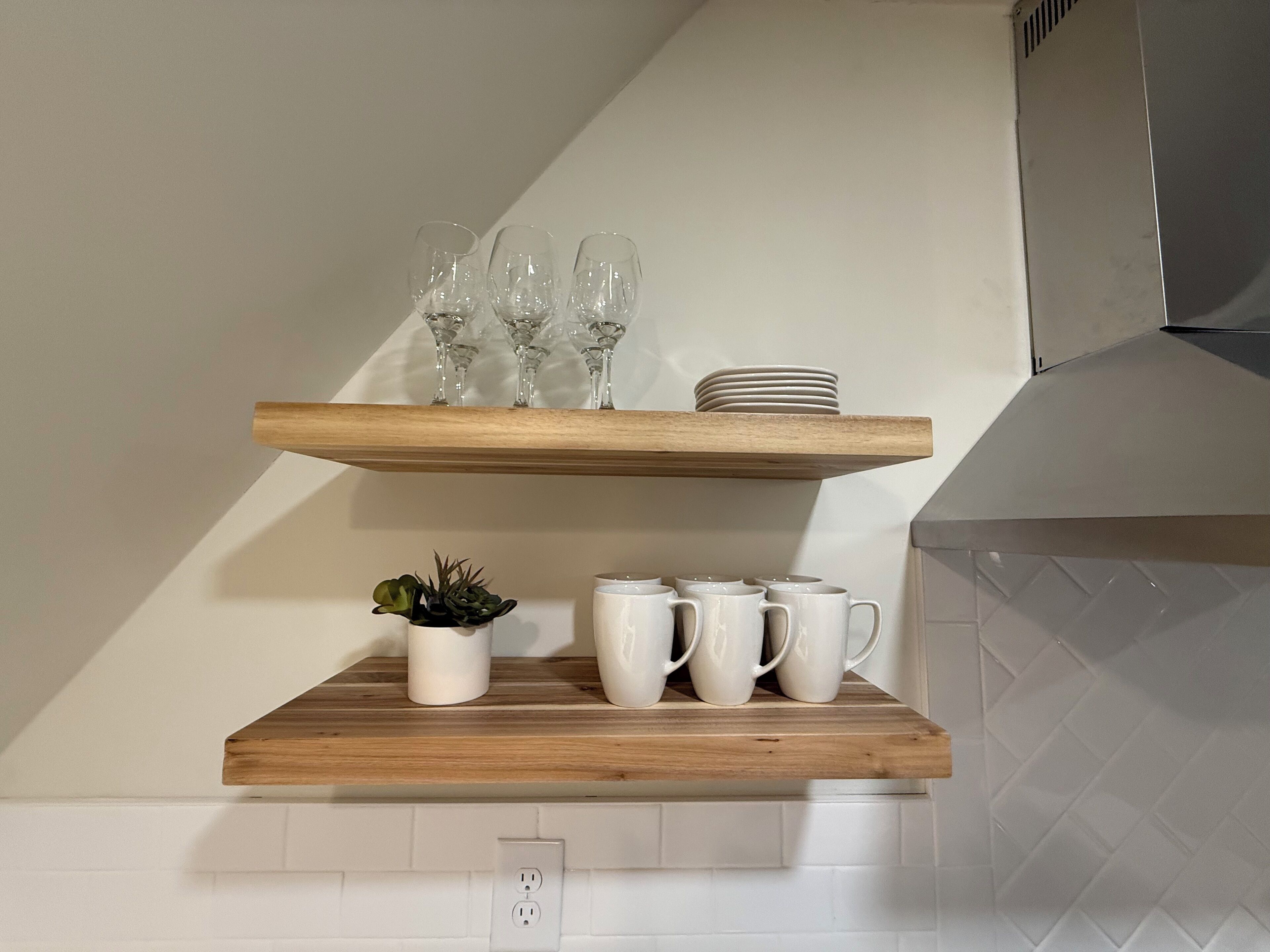 Una cucina con mensole in legno che contengono bicchieri e tazze bianche.