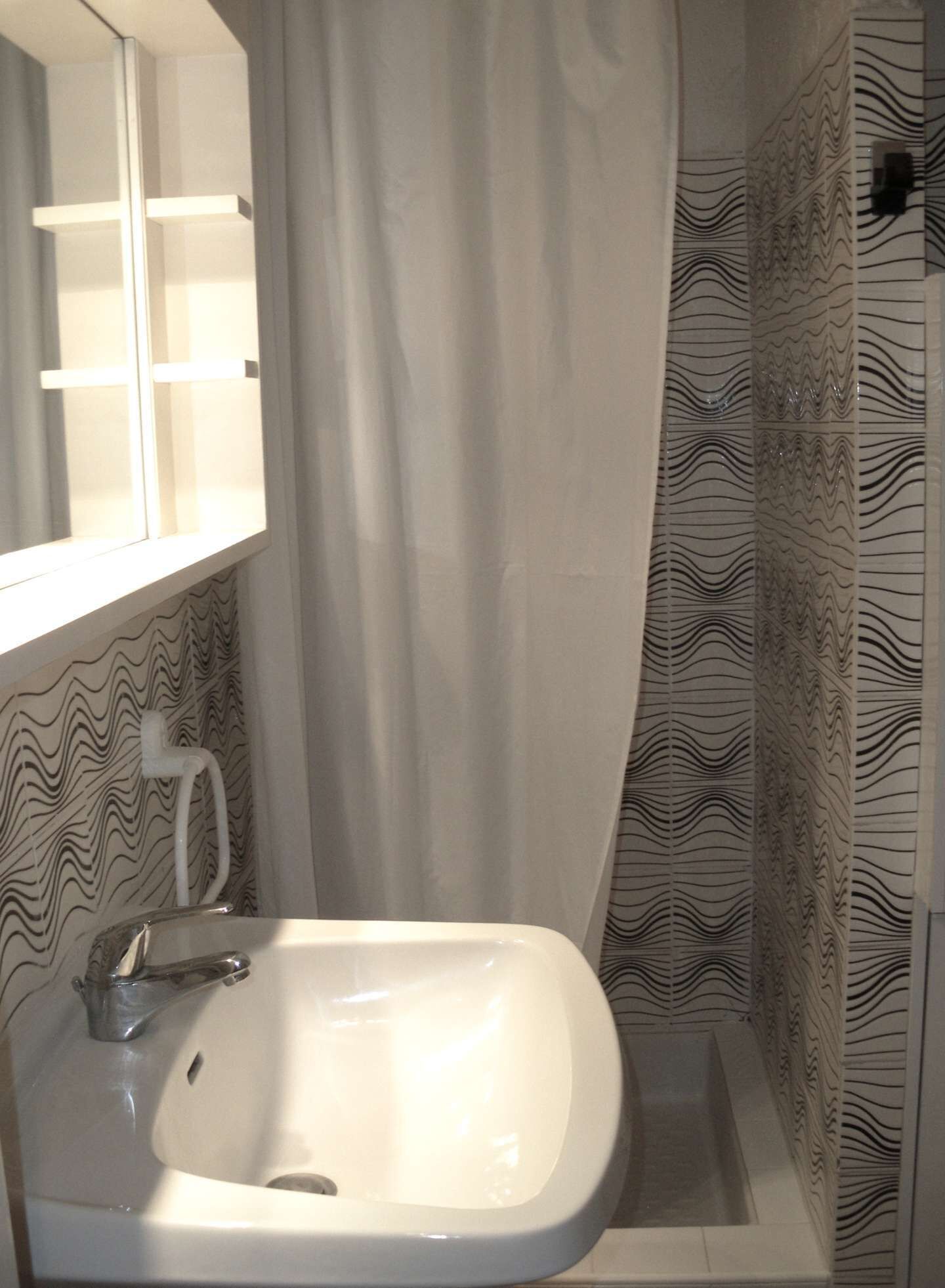 A bathroom with a white sink, a mirror, and a shower with patterned tiles.