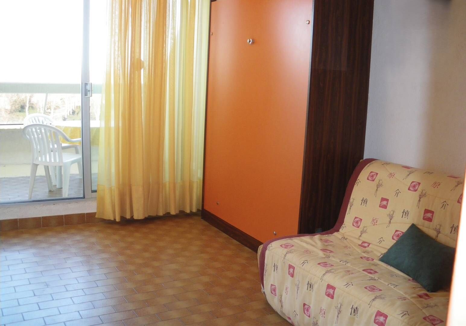 Quarto com sofá, cortina, porta de vidro deslizante e vista para o exterior.