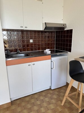 Eine kleine Küche mit weißen Schränken, einer Edelstahl-Spüle und einem kompakten Kühlschrank.
