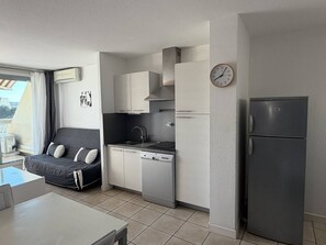 A compact kitchen with a built-in dishwasher, a refrigerator, and a clock on the wall. - PUZZLE - Studio Héliopolis L 86 - Classic - 4 people (AGDE)