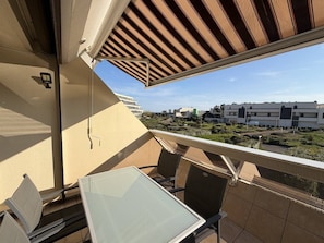 Un balcon avec une table et des chaises en verre, une vue sur un quartier résidentiel et un immeuble au design moderne.