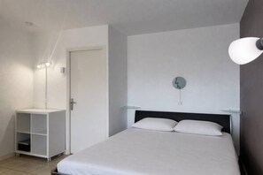 A bedroom with a bed, a bedside table, a wall-mounted lamp, and a door. - PUZZLE - Studio Héliopolis L 86 - Classic - 4 people (AGDE)
